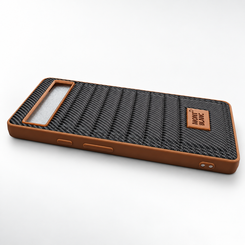 A protective phone case with a brown silicone frame and a textured black carbon-fiber-look backplate, featuring a small brown leather brand patch that reads 'MONT BLANC'.