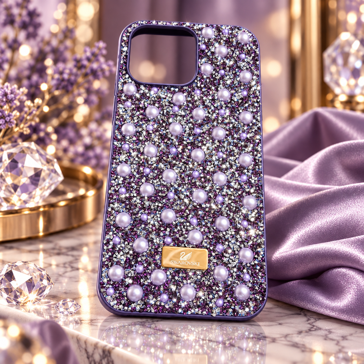 A purple rhinestone 16 pro max phone case decorated with faux pearls and a gold-tone Swarovski logo plaque, displayed on a marble surface with purple and crystal props.