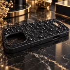 A black phone case embellished with black rhinestones and glossy black beads, resting on a polished black marble surface with gold accents.
